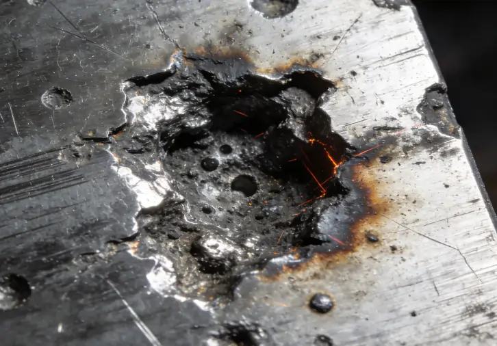 Microscopic view of metal surface damage, melting, and pitting caused by excessive laser power.