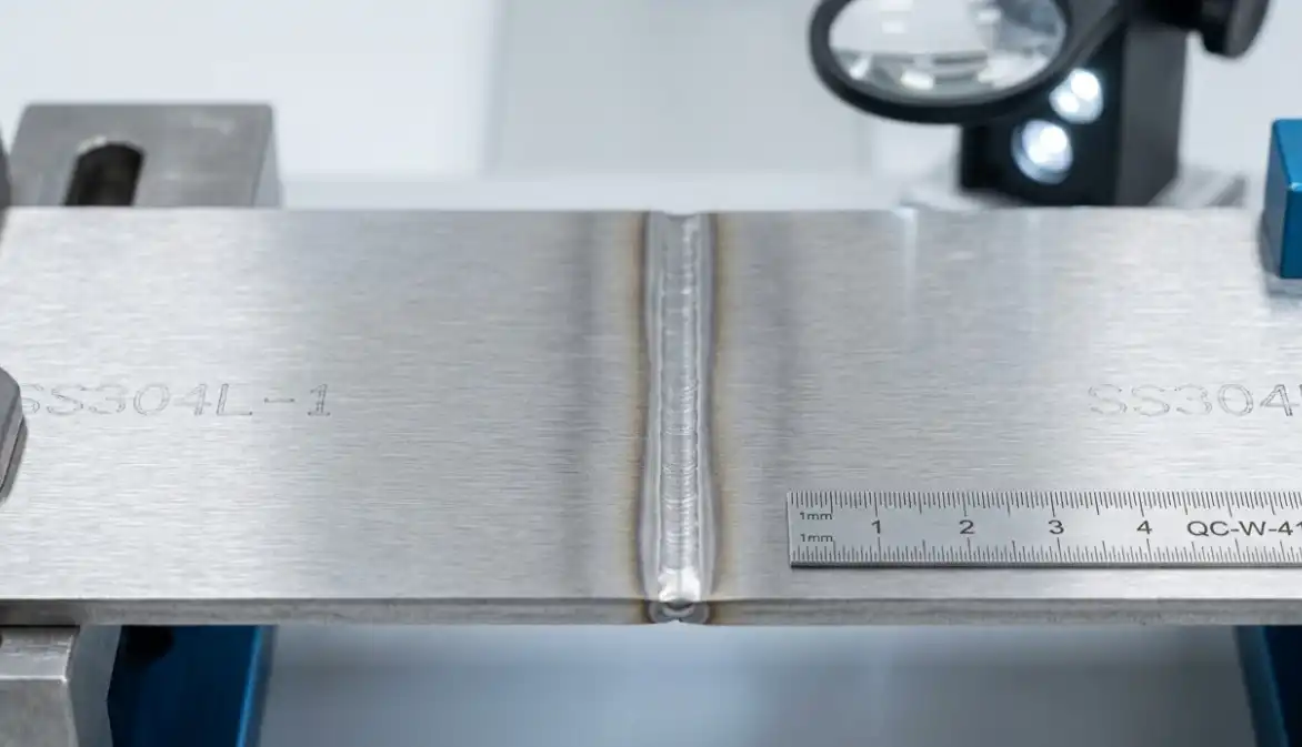 A macro photograph of a perfectly clean and smooth laser weld seam on two pieces of stainless steel joined together without any filler wire (autogenous welding). Industrial quality control context, high resolution.