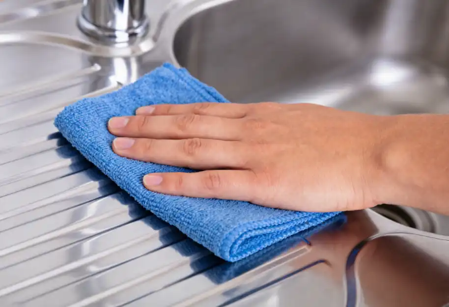Hand wiping a stainless steel sink with a microfiber cloth strictly following the grain direction.