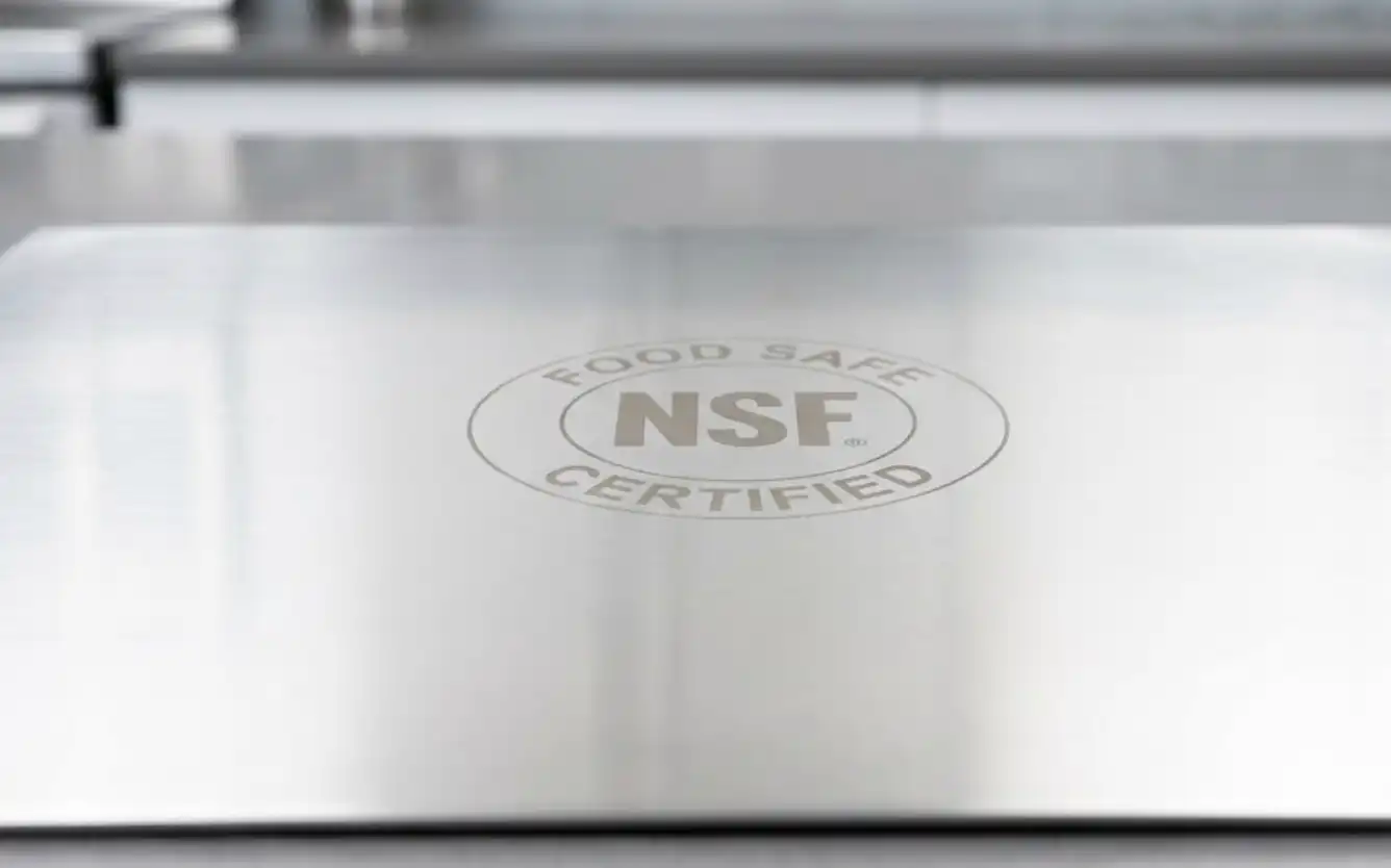 A macro photograph of a pristine, highly polished sheet of food-grade stainless steel. A faint, professional laser-etched 'NSF Certified' or 'Food Safe' logo is visible on the surface. Clean, sterile laboratory or high-end kitchen lighting.