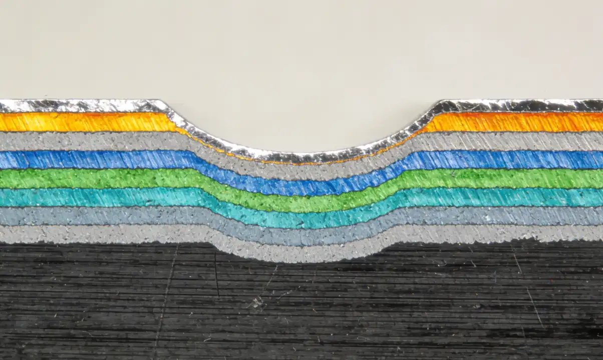 A false-color microscopic cross-section image of hot-dip galvanized steel (metallurgical examination). The image clearly shows the distinct alloy layers formed between the dark steel base at the bottom and the pure zinc coating at the top. Scientific laboratory aesthetic.