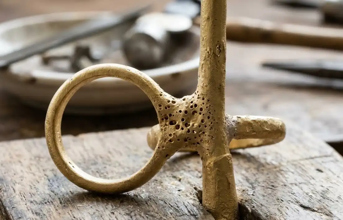 A macro photography close-up of a raw, unfinished 14K yellow gold jewelry casting straight out of the investment mold, showing visible porosity defects (tiny holes and rough surface) on the sprue and ring shank. Sharp focus, highlighting the casting flaws.
