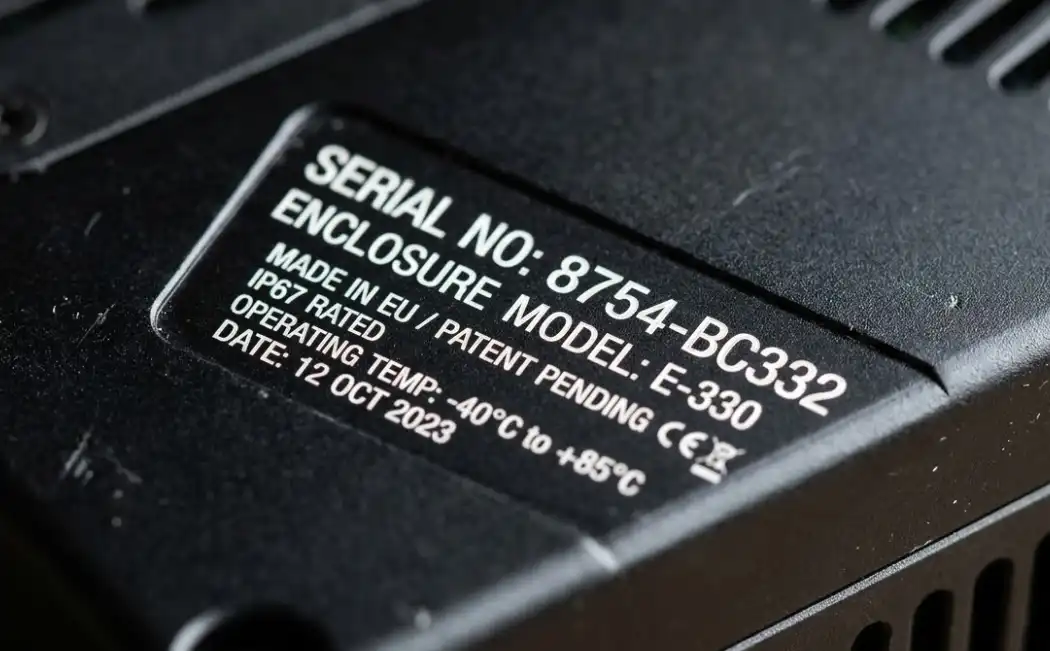 A close-up macro shot of a black anodized aluminum electronic enclosure showing high-contrast, crisp white laser-engraved serial numbers and text, sharp details, industrial aesthetic.